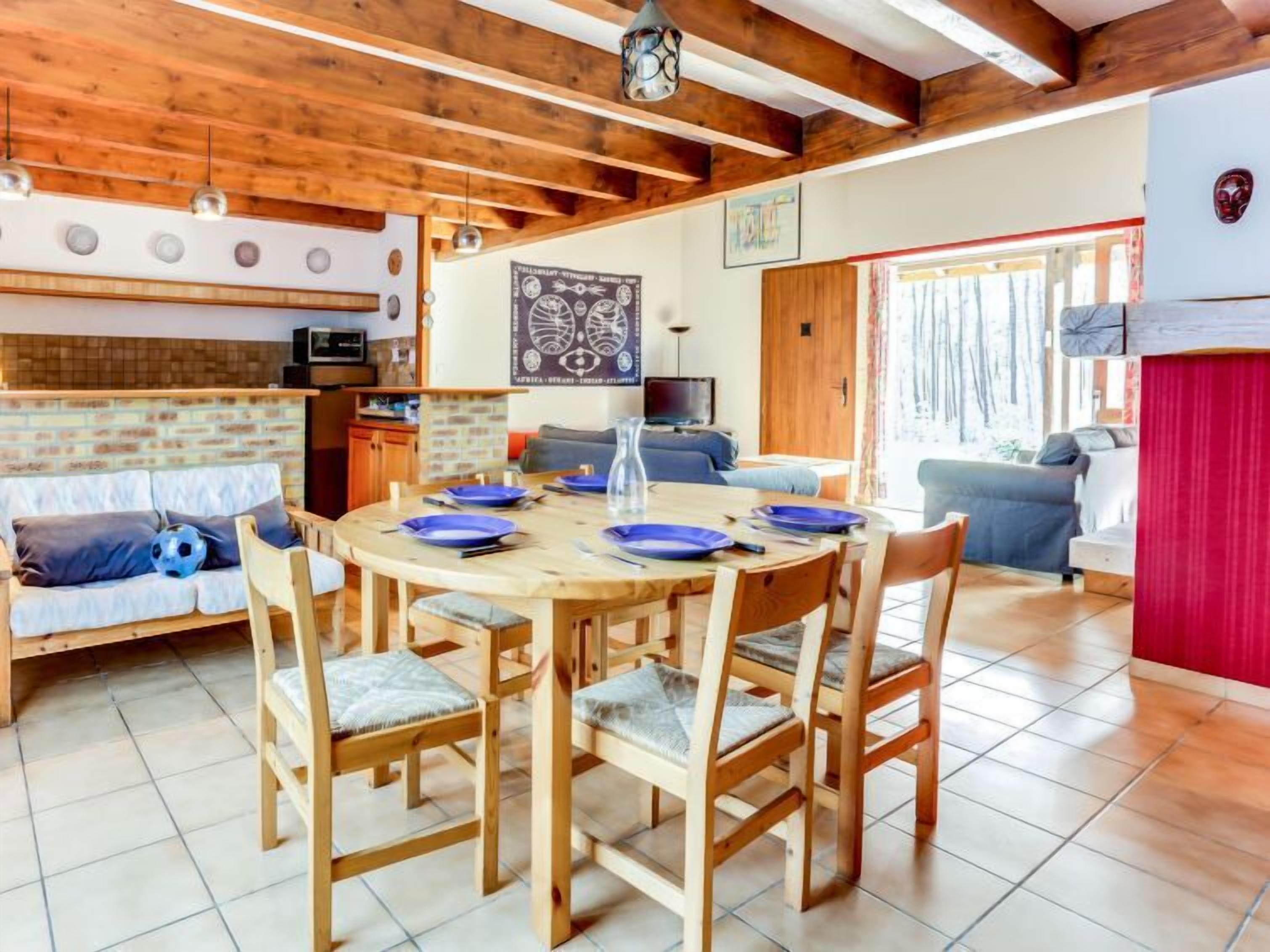 Una sala de estar acogedora con una mesa de madera para comer, sillas y un sofá. Se ve un televisor y una chimenea al fondo.
