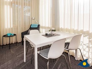 Ein Konferenzraum mit einem weißen Tisch, grauen Stühlen, einem kleinen Beistelltisch mit türkisfarbenen Schalen und einer Lampe.