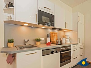 Una cocina moderna con armarios blancos, microondas integrado, cafetera y lavavajillas.
