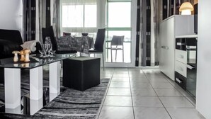 A modern living room with a glass coffee table, black sofa, and a dining area with a table and chairs. There is a large window with curtains, a black ottoman, and a cabinet with drawers. - Schau ins Land (B 97) by Interhome (Dittishausen)