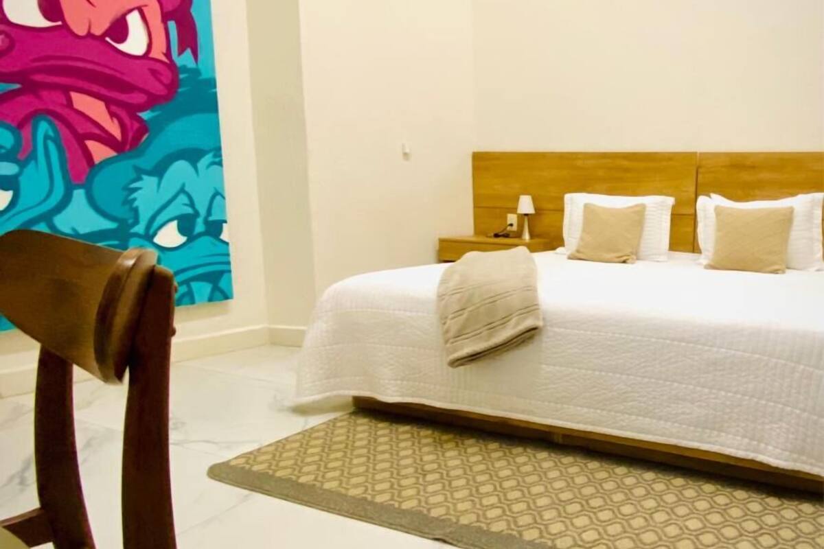 A hotel room with a bed, a headboard, a bedside table, a lamp, and a wall with a colorful mural.