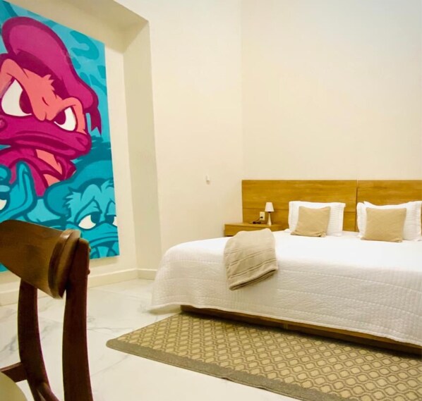 A hotel room with a bed, a headboard, a bedside table, a lamp, and a wall with a colorful mural.