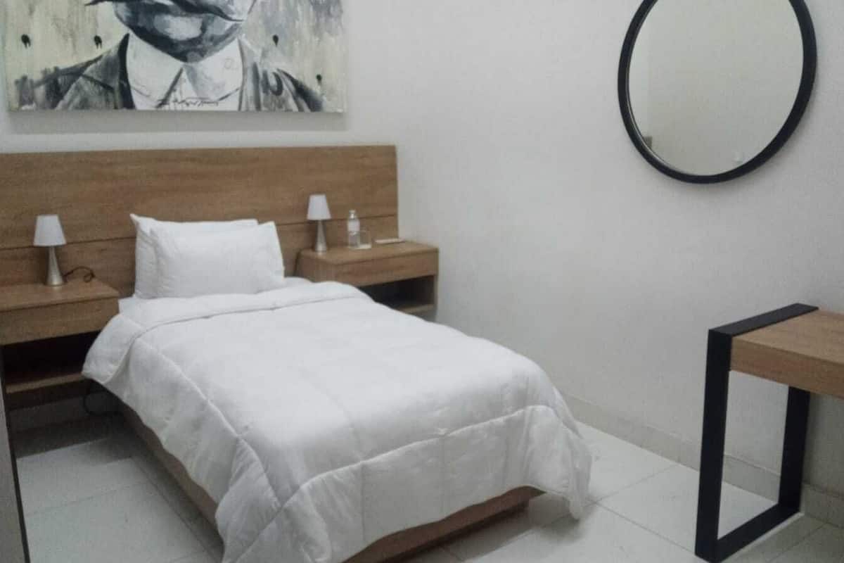 A neatly arranged hotel room with a bed, bedside tables with lamps, a desk, and a round mirror on the wall.