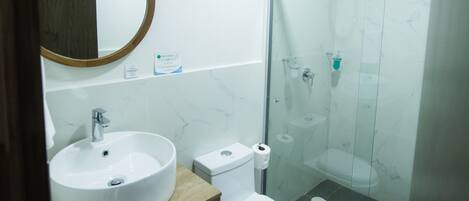 A bathroom with a round mirror, a sink, a toilet, and a glass-enclosed shower.