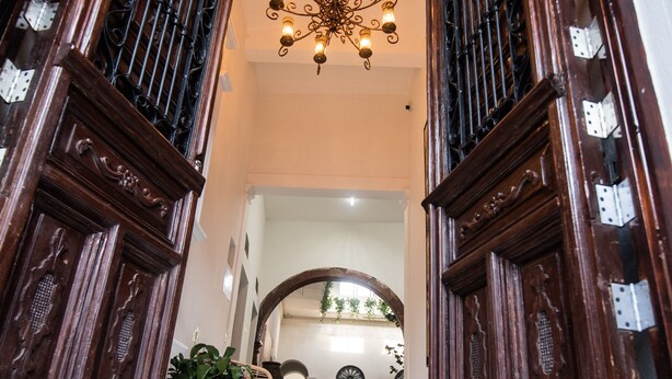 A grand entrance with a chandelier, wooden doors with metal grills, and a marble floor leading to an interior space. - Hotel Via Real (Atotonilco el Alto)