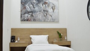 A neatly made bed with a wooden headboard, a bedside table with a water bottle and a small plant, and a painting of horses on the wall. - Hotel Via Real (Atotonilco el Alto)
