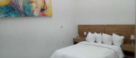 Un dormitorio con una cama, una mesita de noche, una lámpara y un cuadro abstracto y colorido en la pared.