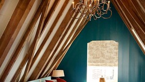 Quarto com teto inclinado, cama com lençóis brancos, almofadas vermelhas, luminária de cabeceira e um lustre.