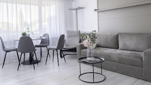 A modern living room with a grey sofa, a round coffee table, and a dining area with a table and chairs.