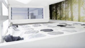 A modern bedroom with a skylight, a bed with a geometric patterned bedspread, and a forest-themed wall mural.