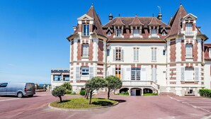 Un grand bâtiment historique à étages, doté d’une entrée principale et d’une allée menant à un parking où est garé un fourgon.