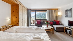 Quarto de hotel com duas camas, um sofá, uma TV e vista para montanhas.
