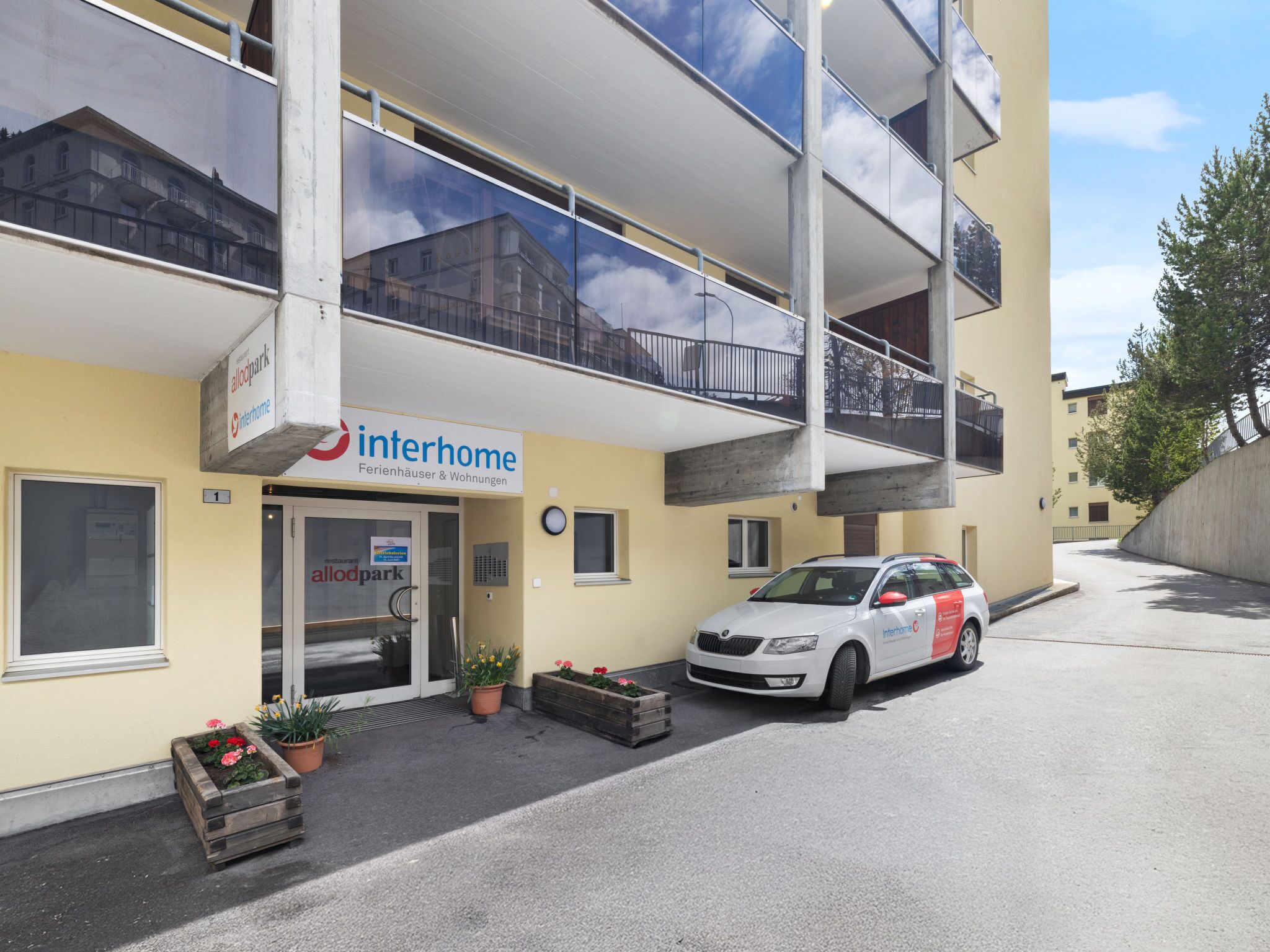 Un edificio a due piani con balconi, un'auto parcheggiata davanti e piante in vaso.