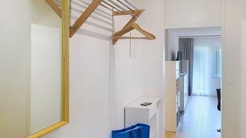 Un couloir avec un étendoir en bois, un miroir, une armoire blanche et un sac bleu.