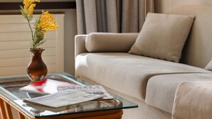 Un salon avec une table basse en verre, un canapé beige et un vase rempli de fleurs jaunes.