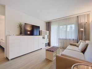 Uma sala de estar moderna com uma televisão de tela plana, um sofá, uma mesa de centro e uma estante de livros.