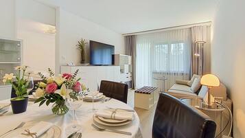 A hotel room with a dining area, a TV, a sofa, and a lamp.