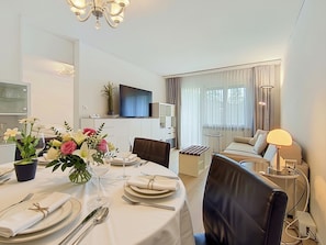 Quarto de hotel com área de jantar, televisão, sofá e luminária.