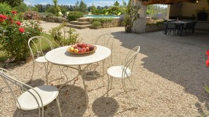 Eine Terrasse mit einem runden Tisch und Stühlen, einer Obstschale und einem Pool im Hintergrund.