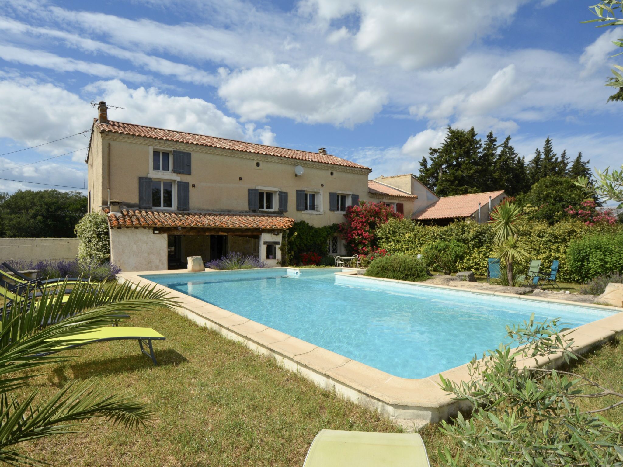 Une maison à deux étages avec une piscine, entourée de verdure et sous un ciel dégagé.