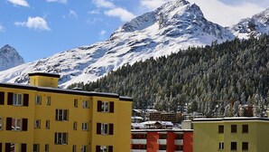 A yellow building with multiple windows, a red building with a similar window arrangement, and a mountain range in the background. - Chesa Fleury by Interhome (St. Moritz)