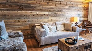 A living room with a wooden wall, a grey sofa, a fur chair, and a wooden coffee table. - Chesa Fleury by Interhome (St. Moritz)