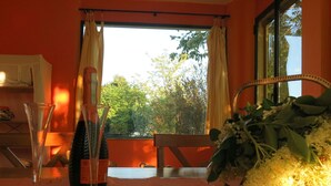 A table with a bottle, glasses, and a floral arrangement in a room with a window and orange walls. - Vacation home Busani by Interhome (Salsomaggiore Terme)