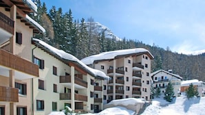 A multi-story hotel with balconies, snow-covered roofs, and a mountainous backdrop. - Residenza Chesa Margun 710-4 by Interhome (Silvaplana-Surlej)