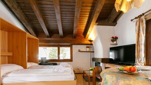 A cozy room with wooden bunk beds, a television, a dining table with fruit, and a window with a view of greenery. - Residenza Chesa Margun 710-4 by Interhome (Silvaplana-Surlej)
