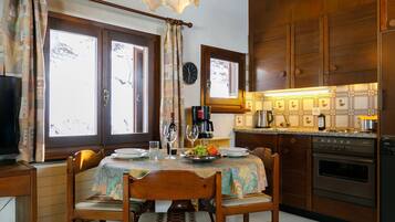 Une cuisine avec des meubles de rangement en bois, une table à manger avec des chaises, une horloge et une fenêtre avec des rideaux.