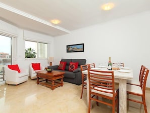 Un salon comprenant un canapé, deux fauteuils, une table basse et une table à manger dressée pour quatre personnes.