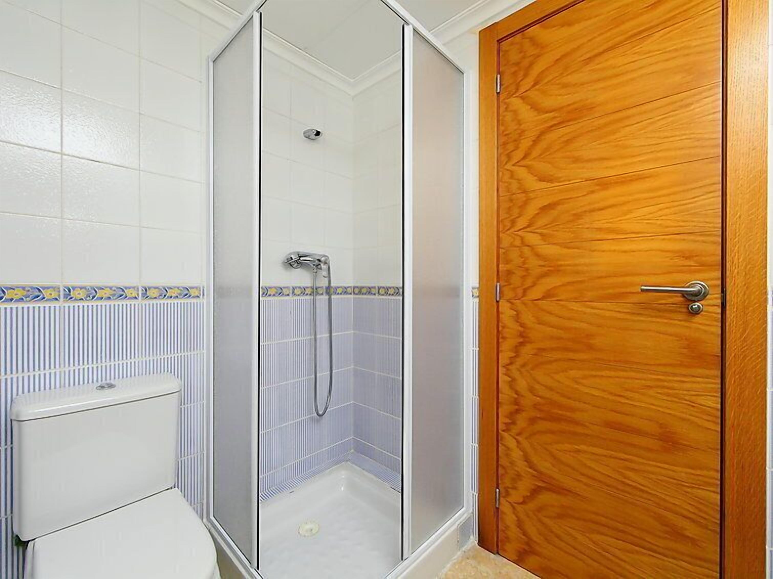 Un bagno con un WC, una doccia con porta in vetro e una porta in legno.