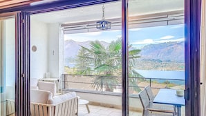 A balcony with a view of mountains and a lake, a table, chairs, and a sofa.