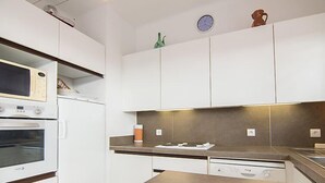 A modern kitchen with white cabinets, a built-in oven, a microwave, a sink, and a stove. There is a magazine on the counter. - Riva Bella by Interhome (Cavalaire)