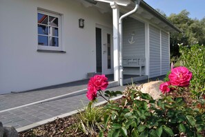A white building with a porch, a window, and a rock in the foreground.