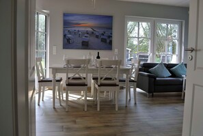 A dining area with a table and chairs, a sofa, and a beach scene painting on the wall.