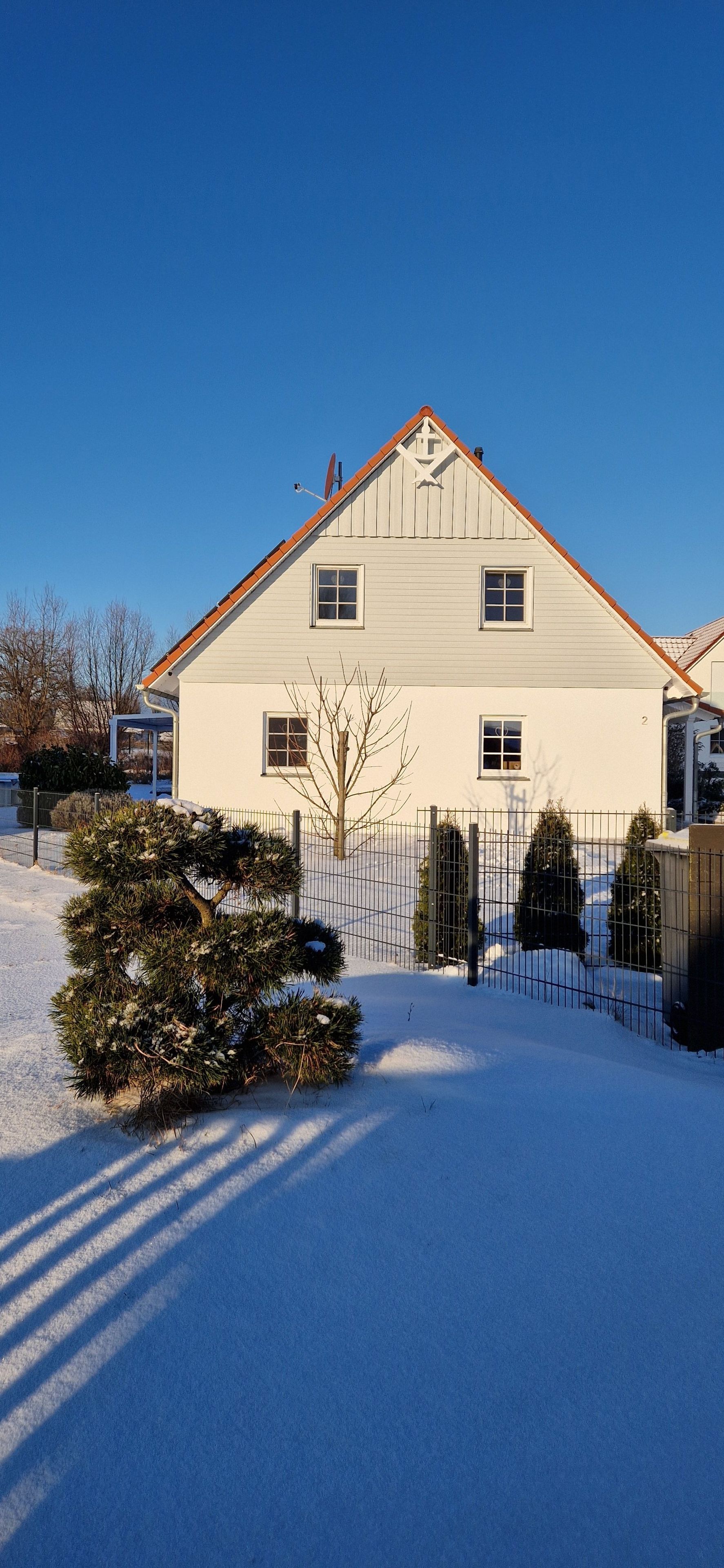 A two-story building with a sloped roof, a fenced yard, and a snow-covered ground.