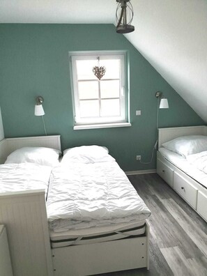 A bedroom with two beds, a window with a decorative item, and two wall-mounted lamps.