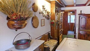 Une cuisine rustique avec des poutres en bois, une table blanche et un pot suspendu contenant des plantes séchées.