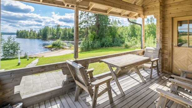 A wooden deck with a table and benches overlooking a lake and forest.
