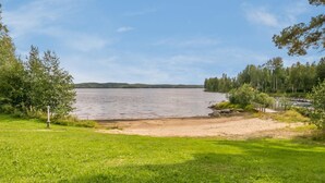 A lakeside view with a grassy area, a wooden bridge, and trees in the background.