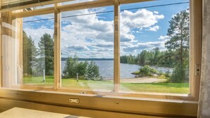 A room with a large window offering a view of a lake, surrounded by trees and a grassy area.