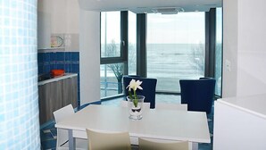 A modern dining area with a white table and chairs, a vase with a white flower, and a view of the sea through large windows. - Appartamento 2 by Interhome (Terracina)