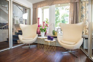 Ein Zimmer mit zwei Ledersesseln, einem kleinen Tisch mit Blumenvase und einem Fenster mit Vorhängen.