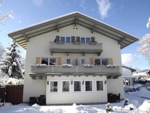 A two-story building with a balcony on the upper floor, a covered entrance, and a snow-covered landscape. - Double Room 2 - Hotel Berlin Tegernsee Garni (Rottach-Egern)