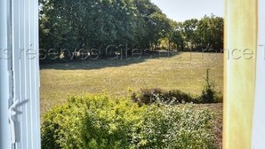 A view from a window overlooking a grassy field with trees in the background. - Comfortable cottage with large private garden and WIFI (Channay-sur-Lathan)