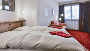 A hotel room with a large bed, a chair, a desk, and a window with curtains. - Chalet Abendrot apARTments by Interhome (Grindelwald)