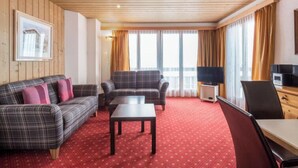 A hotel room with a wooden ceiling, a red carpet, two sofas, a coffee table, a TV, and a desk with a chair. - Chalet Abendrot apARTments by Interhome (Grindelwald)