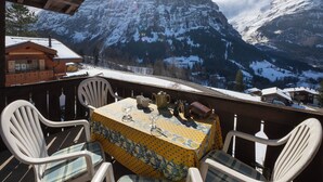 Une table entourée de chaises sur un balcon donnant sur des montagnes enneigées.