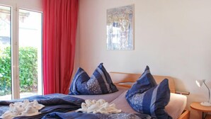 Una habitación de hotel con una cama, una ventana con cortinas rojas, un cuadro en la pared y una pequeña mesa con una lámpara.